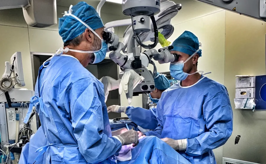 Intervento in sala operatoria: due chirurghi in camice e cuffia azzurri lavorano al microscopio operatorio